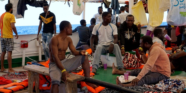 Migrants sit on the deck of the Open Arms vessel in front of island of Lampedusa as crew members described the situation on board as ''desperate,'' saying that a man threw himself in the water trying to reach land in plain view, while at the same moment a woman suffered a panic attack. (AP Photo/Francisco Gentico)