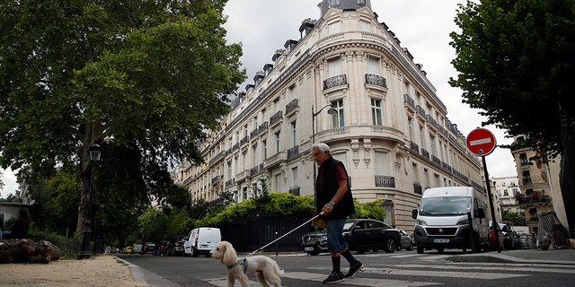 A man walks his dog next to an apartment building owned by Jeffrey Epstein in the 16th district in Paris, Tuesday, Aug. 13, 2019. France's government wants prosecutors to open an investigation into Jeffrey Epstein's links to France following his death in a Manhattan jail cell. U.S. authorities say Epstein had a residence in Paris and used a fake Austrian passport to travel to France in the 1980s.