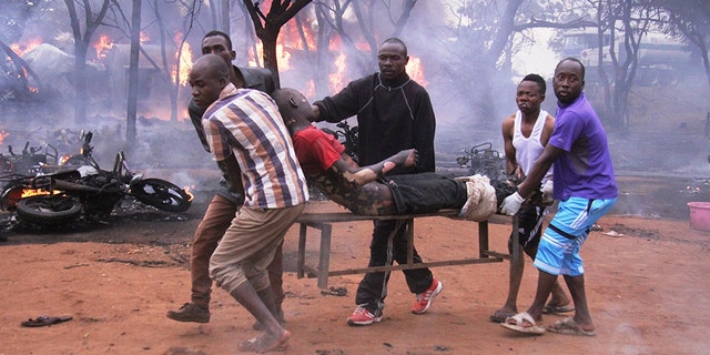 An injured man is carried from the scene as a petrol tanker burns in the background. (AP Photo)