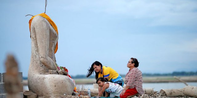 A family prays near the ruins of a headless Buddha statue that resurfaced in a dried-up dam because of a drought in Lopburi, Thailand, on Aug. 1, 2019. (Credit: Soe Zeya Tun/Reuters/Newscom)