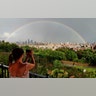 A woman photographs a rainbow after it formed following a thunderstorm over the skyline of midtown Manhattan in New York City, Aug. 21, 2019. 