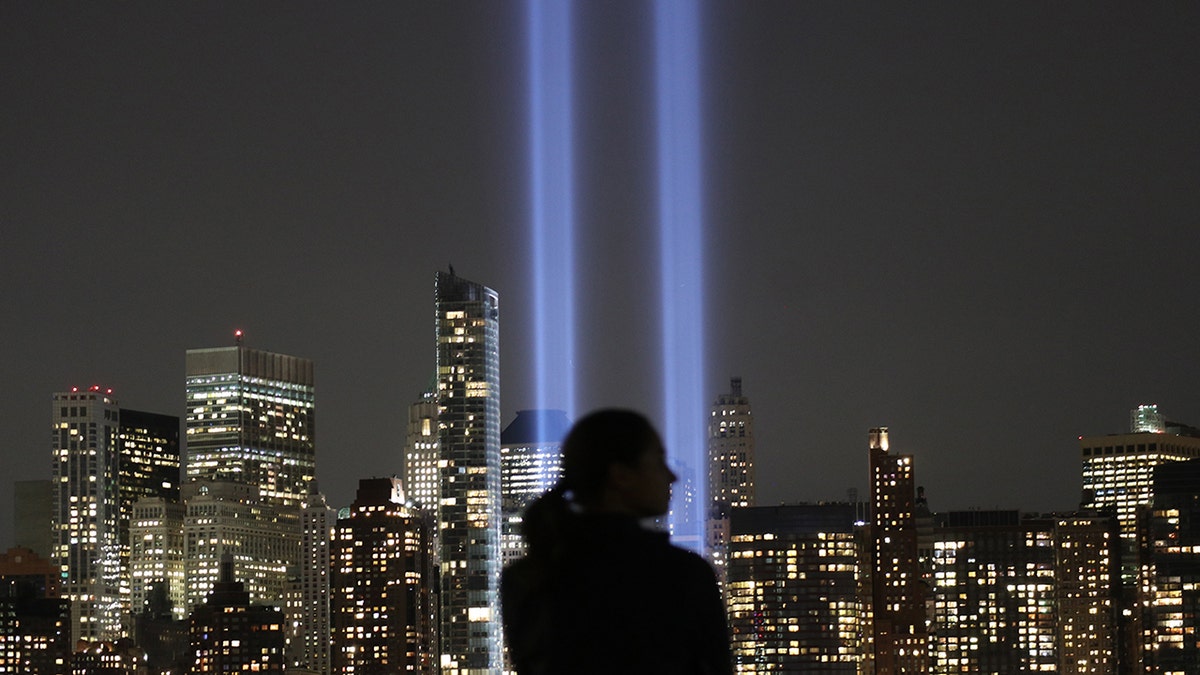 A person is standing in the dark watching two strobe lights blaring in the sky to indicate the twin towers