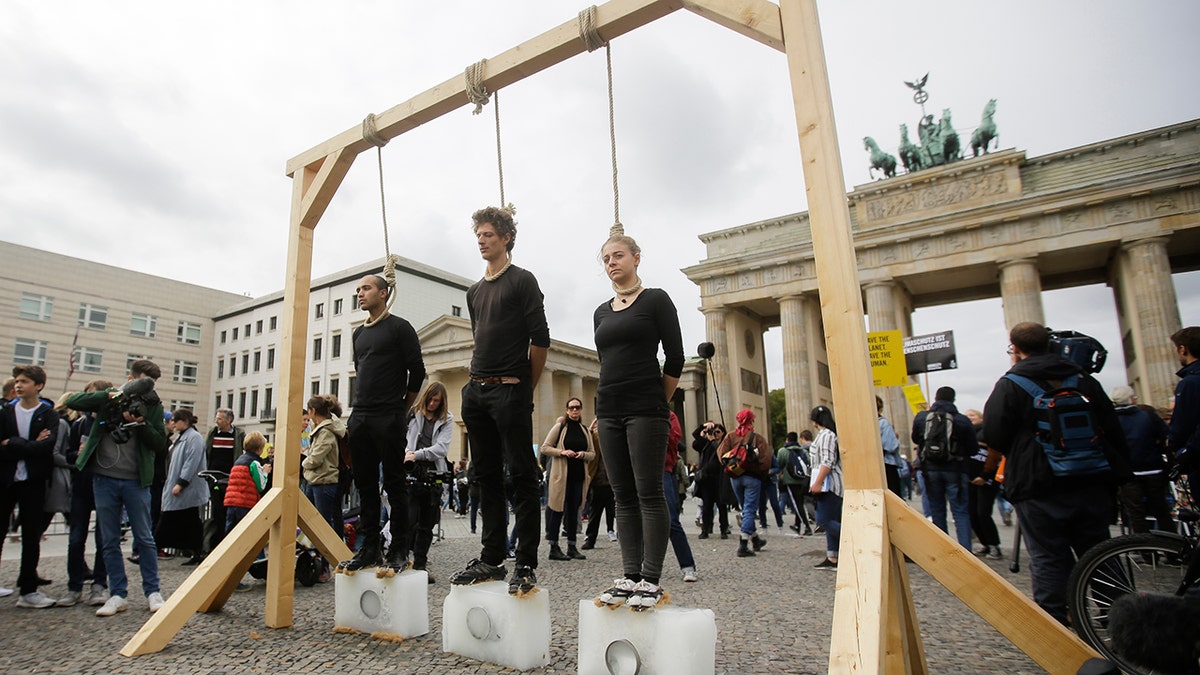 Three persons stand on ice blocks under gallows to protest against the climate policy prior to a 'Friday for Future' climate protest in front of the Brandenburg Gate in Berlin, Germany, Friday, Sept. 20, 2019.?