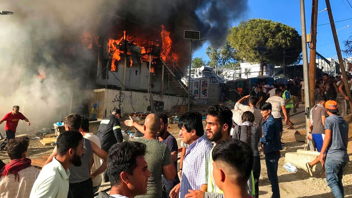 Migrants and refugees stand next to burning house containers at the Moria refugee camp, on the northeastern Aegean island of Lesbos, Greece, Sunday, Sept. 29, 2019. 