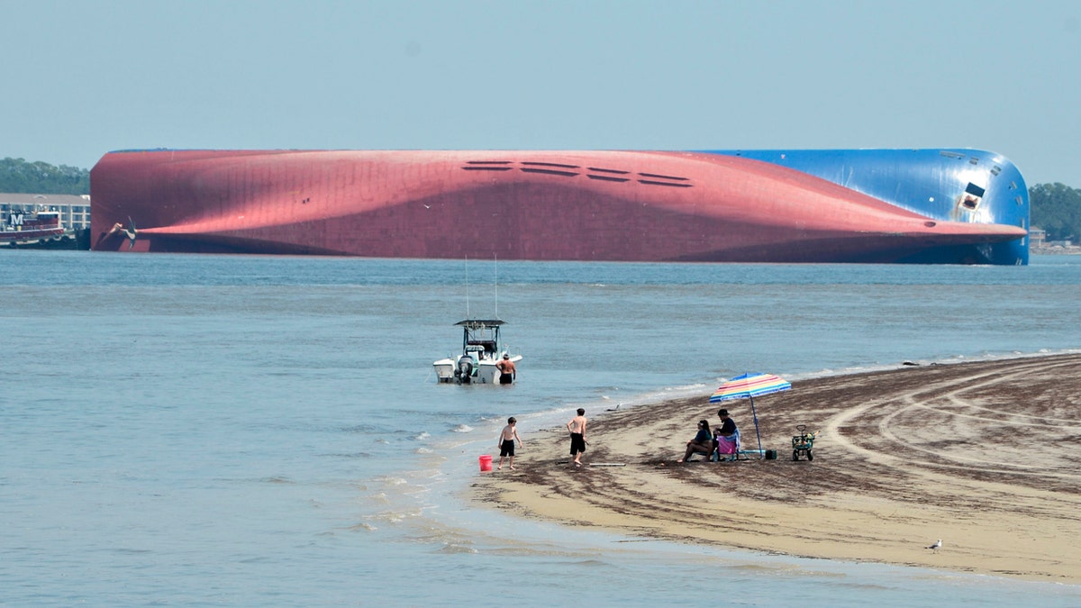 People are shown on Jekyll Island's Driftwood Beach as the Golden Ray cargo ship is capsized in the background, off the Georgia coast, Sunday, Sept. 8, 2019.