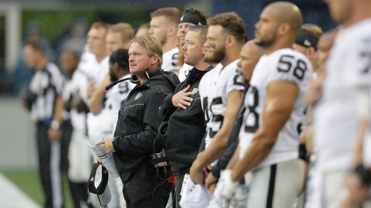 Oakland Raiders head coach Jon Gruden, center, stands with his players during the singing of the national anthem before an NFL football preseason game against the Seattle Seahawks, Thursday, Aug. 29, 2019, in Seattle. (AP Photo/Stephen Brashear)