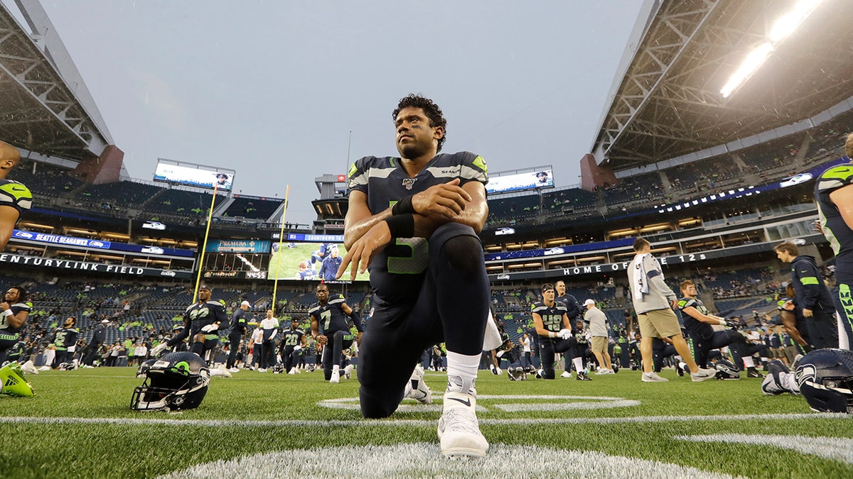 Seattle Seahawks quarterback Russell Wilson kneels on the field as he stretches before an NFL football preseason game against the Oakland Raiders, Thursday, Aug. 29, 2019, in Seattle. (AP Photo/Elaine Thompson)