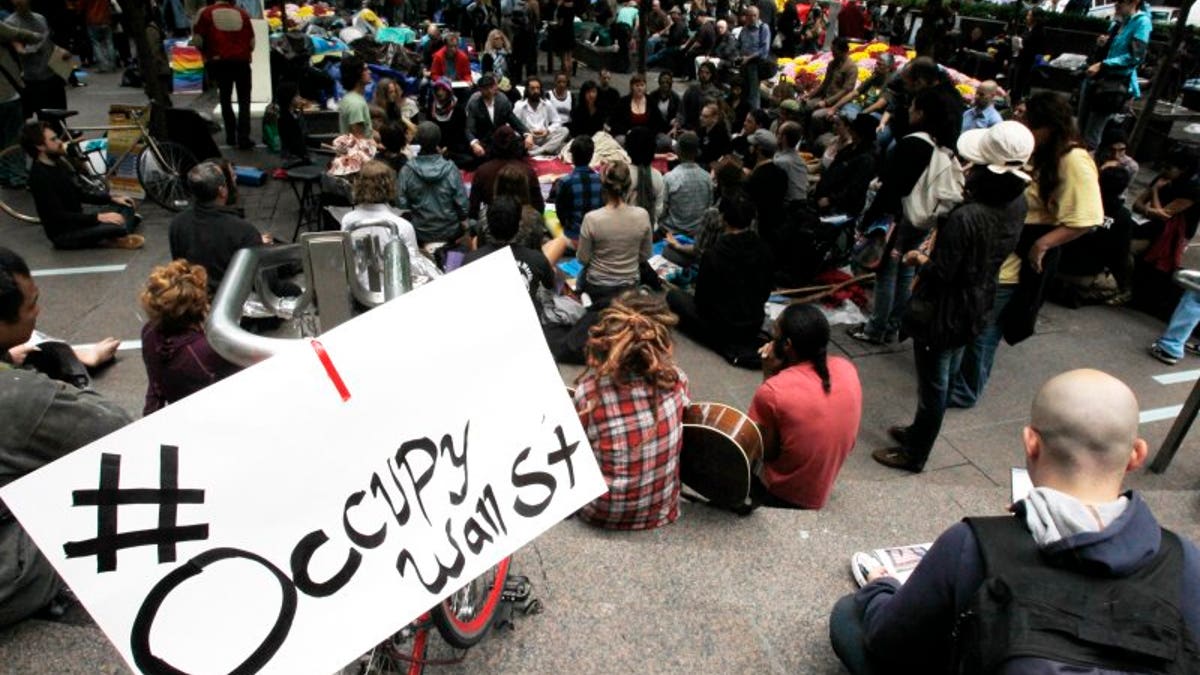 FILE – Occupy Wall Street protesters meditate while a sign bearing their twitter handle hangs from a railing in Zuccotti Park in New York October 1, 2011. REUTERS/Jessica Rinaldi