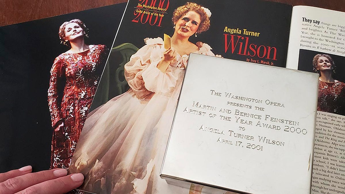 In this Tuesday, Sept. 2, 2019 photo provided by opera singer Angela Turner Wilson, she displays her 2000 Artist of the Year award from the Washington Opera next to a photo of herself from a 1999 performance of 