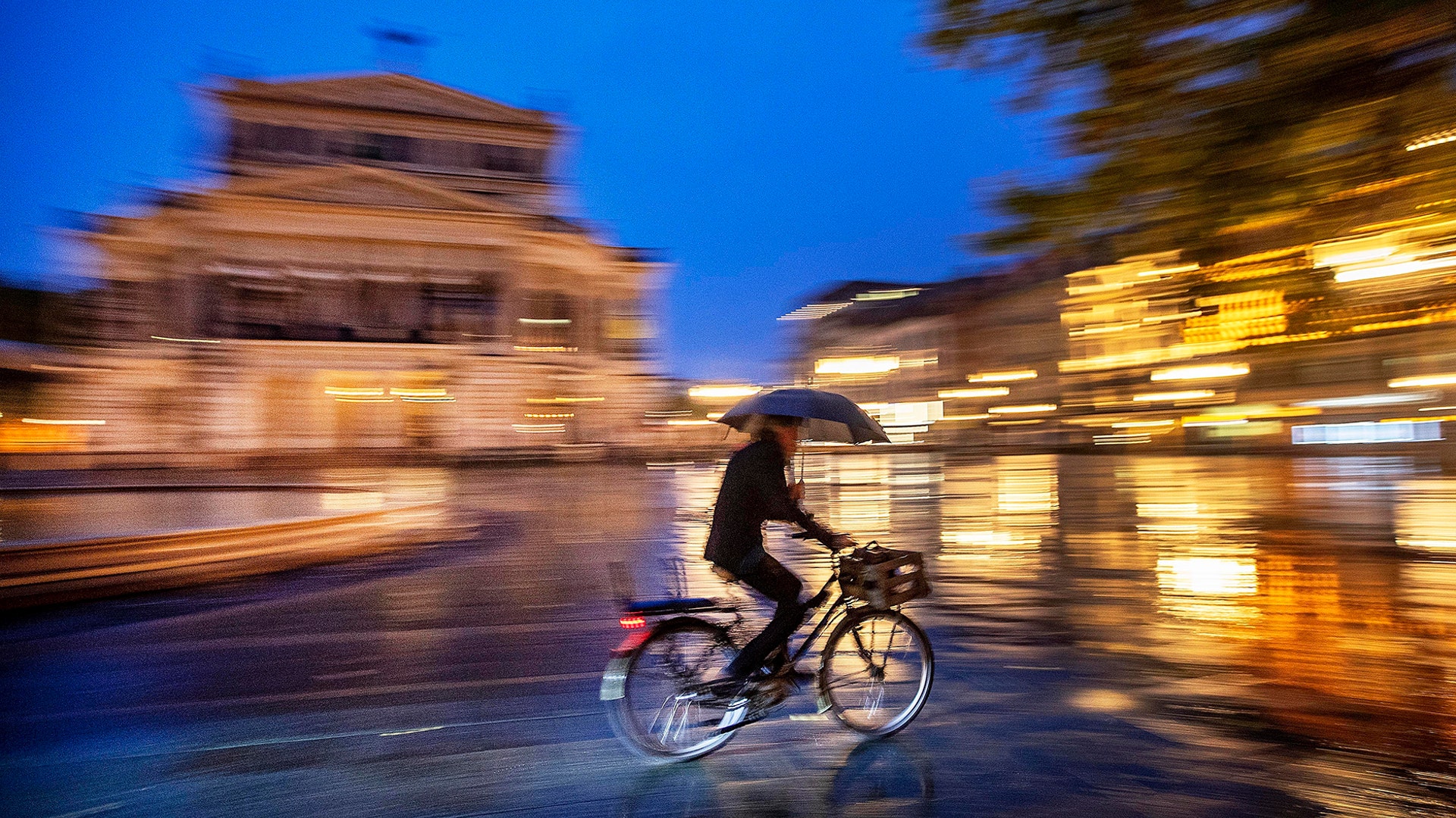 A man with an umbrella rides his bike in front of the Old Opera House in Frankfurt, Germany, Sept. 23, 2019.
