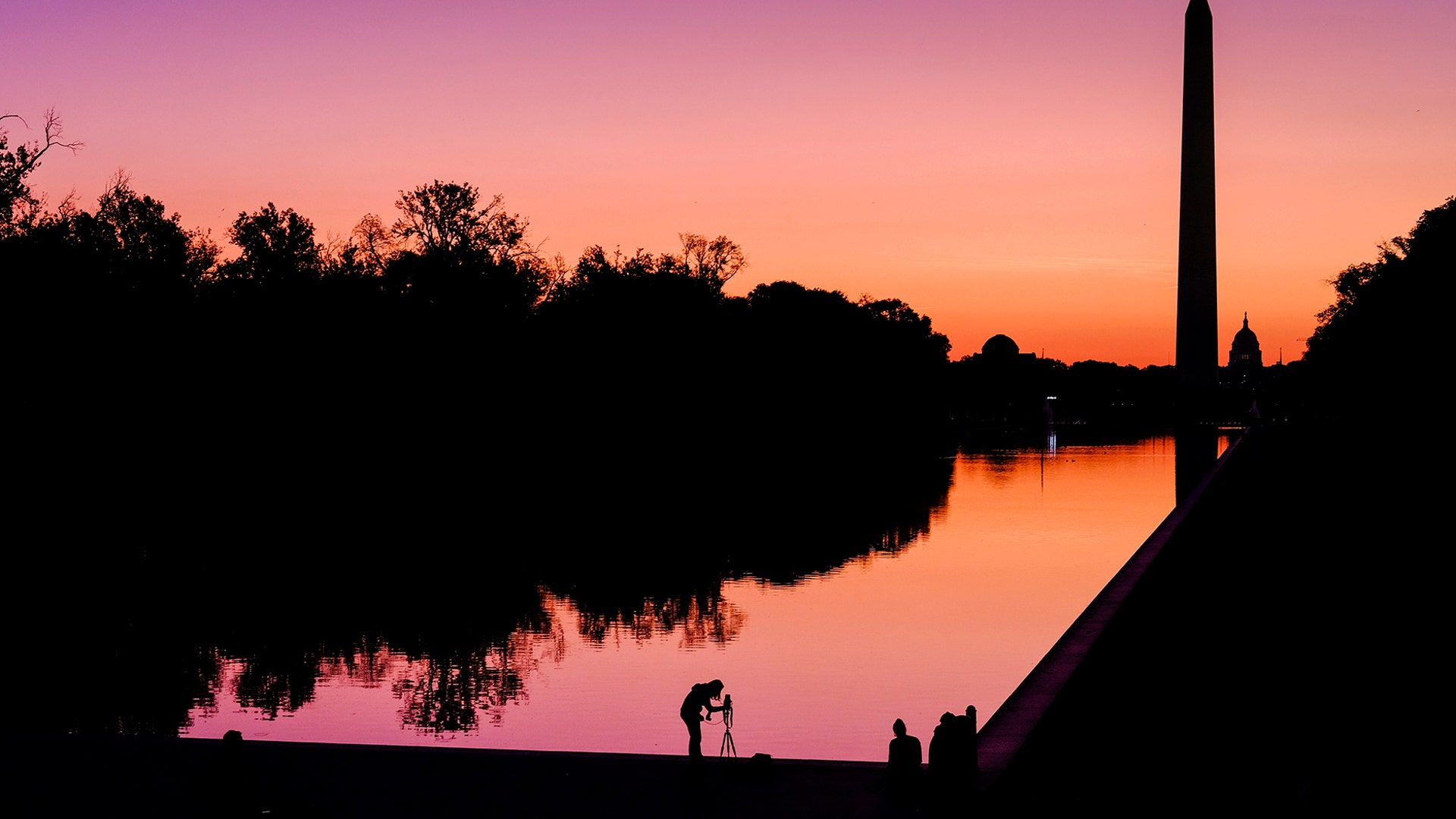 A photographer lines up her shot at the National Mall reflecting pool as the sun begins to rise behind the Washington Monument and the U.S. Capitol building in Washington, Sept. 21, 2019. 