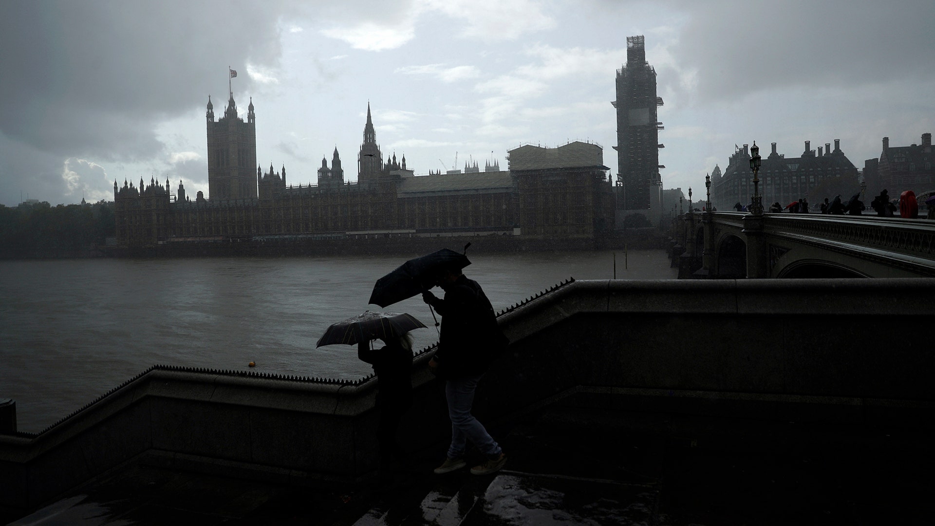 People are silhouetted with umbrellas in the rain backdropped by the Houses of Parliament in London, Sept. 24, 2019. 