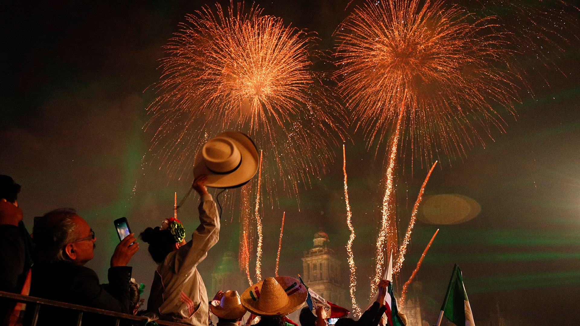 Revelers celebrate as fireworks explode over the Metropolitan Cathedral to kick off Independence Day celebrations in Mexico City, Sept. 15, 2019. 