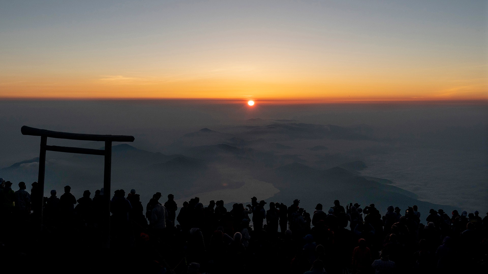 People gather around a torii gate as they watch the sunrise from the summit of Mount Fuji in Japan, Aug. 3, 2019. 