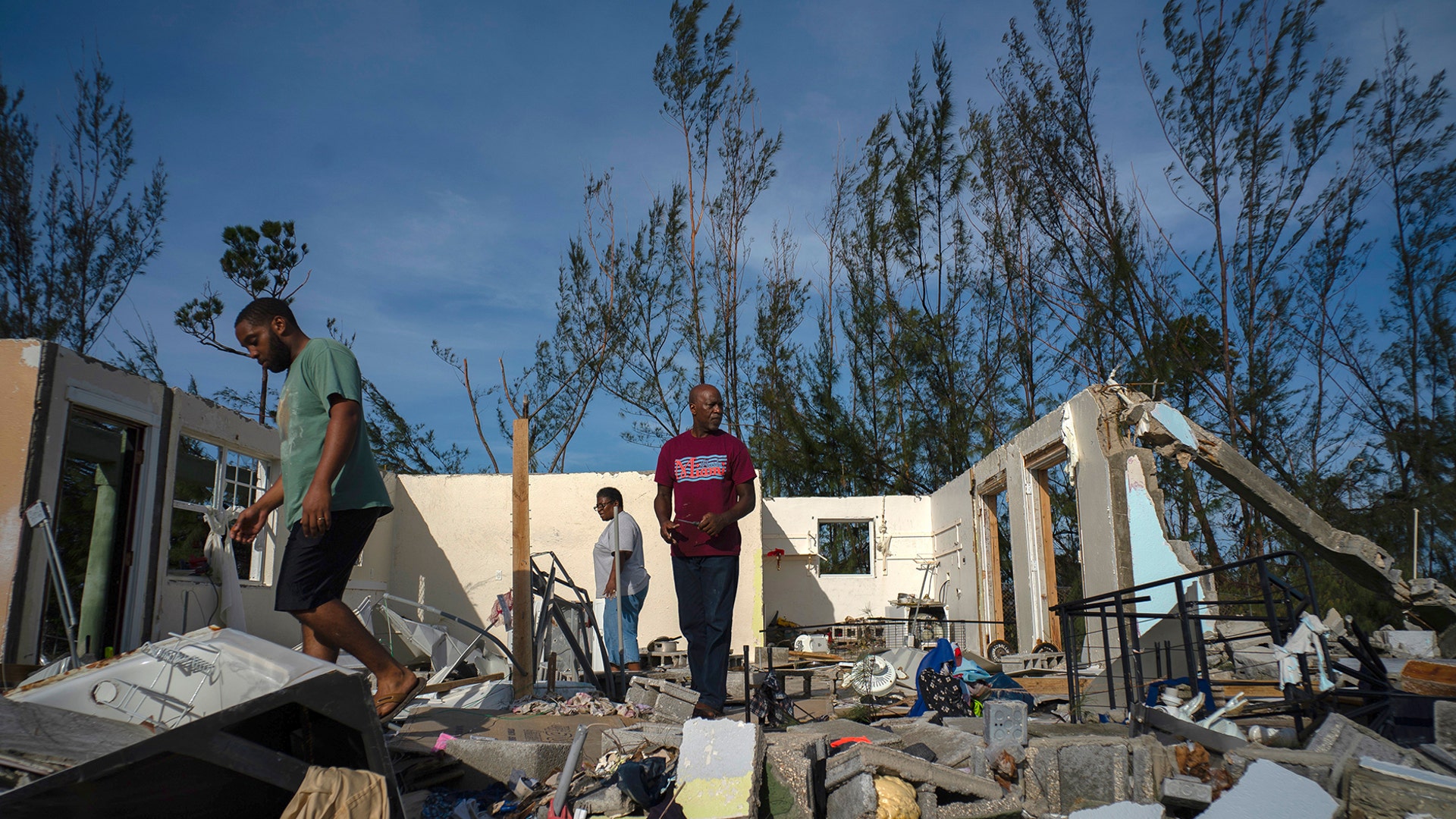 George Bolter and his parents walk through the remains of his home destroyed by Hurricane Dorian in the Pine Bay neighborhood of Freeport, Bahamas, Sept. 4, 2019.