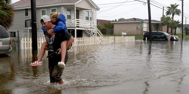 Terry Spencer carries his daughter, Trinity, through high water on 59th Street near Stewart Road in Galveston, Texas. (Jennifer Reynolds/The Galveston County Daily News via AP)
