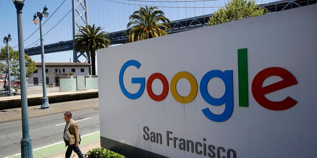 FILE - In this May 1, 2019, file photo a man walks past a Google sign outside with a span of the Bay Bridge at rear in San Francisco. A group of states are expected to announce an investigation into Google on Monday, Sept. 9, to investigate whether the tech company has become too big. (AP Photo/Jeff Chiu, File)