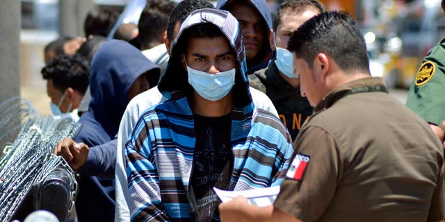 In this July 25, 2019, file photo, Mexican officials and United States Border Patrol officers return a group of migrants to the Mexico side of the border as Mexican immigration officials check a list in Nuevo Laredo, Mexico.  