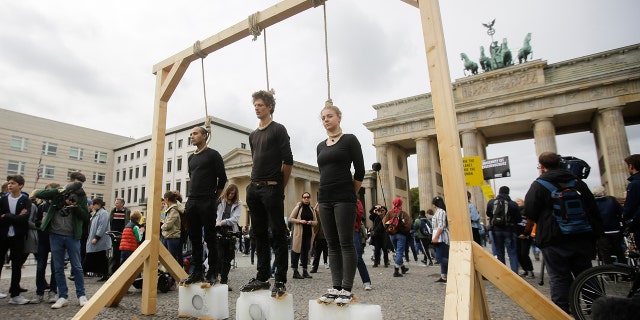 Three persons stand on ice blocks under gallows to protest against the climate policy prior to a 'Friday for Future' climate protest in front of the Brandenburg Gate in Berlin, Germany, Friday, Sept. 20, 2019.