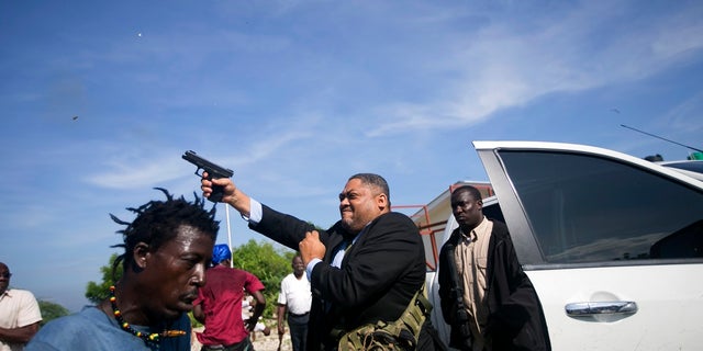 Ruling party Sen. Ralph Fethiere fires his gun outside Parliament as he arrives for a ceremony to ratify Fritz William Michel's nomination as prime minister. (AP Photo/Dieu Nalio Chery)