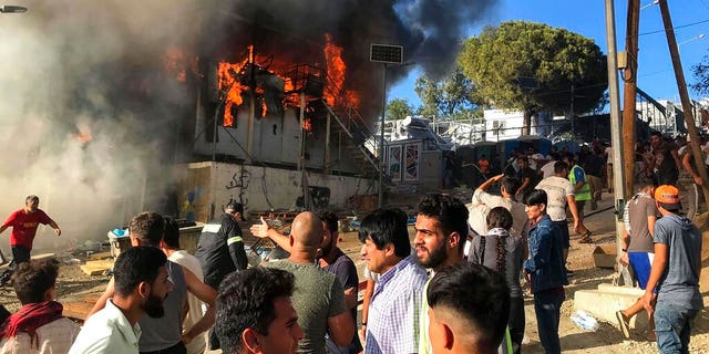 Migrants and refugees stand next to burning house containers at the Moria refugee camp, on the northeastern Aegean island of Lesbos, Greece, Sunday, Sept. 29, 2019. 