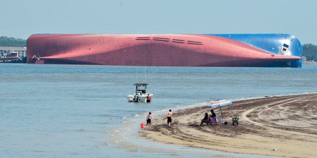 People are shown on Jekyll Island's Driftwood Beach as the Golden Ray cargo ship is capsized in the background, off the Georgia coast, Sunday, Sept. 8, 2019.