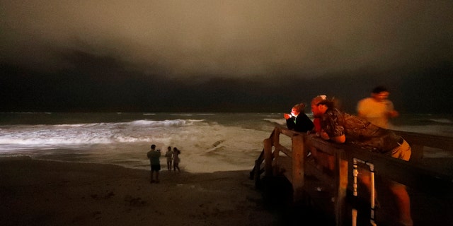 People stand on the boardwalk along the Atlantic Ocean at night as the outer bands of Hurricane Dorian reach Vero Beach, Fla., Monday, Sept. 2, 2019.