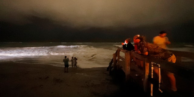 People stand on the boardwalk along the Atlantic Ocean at night as the outer bands of Hurricane Dorian reach Vero Beach, Fla., Monday, Sept. 2, 2019.