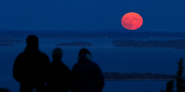 Jack and Kathy Duepree of Camden, Maine, and their friend Betsy Starman of Naples, Florida, watch the nearly full harvest moon rise on Penobscot Bay on Friday.