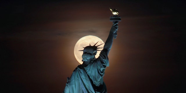 Friday the 13th of the harvest moon rises behind the Statue of Liberty.