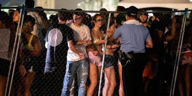 In this Saturday, Sept. 7, 2019 photo, Festival-goers talk to a police officer after they try to jump the fence during Lil Wayne's fifth annual Lil WeezyAna Fest at the UNO Lakefront Arena grounds in New Orleans. A crowd stampede injured several people attending a New Orleans festival organized by rapper Lil Wayne.