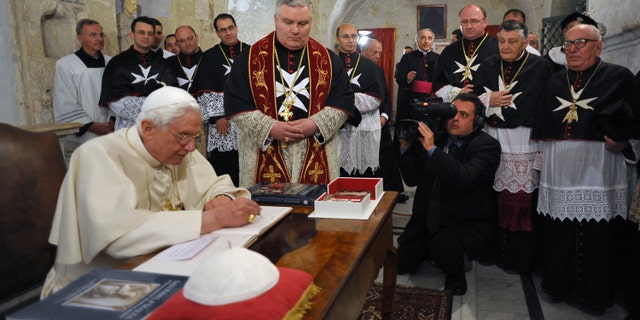 This handout picture released on April 17, 2010 by The Vatican press office shows Pope Benedict XVI (L) signing a book while Malta's knights watch at Saint Paul's Grotto in Rabat, on the first day of his trip to Malta. The grotto located in Rabat, in the center of the archipelago's main island, is the place where the apostle Paul took refuge after his shipwreck on Malta, according to Christian tradition.