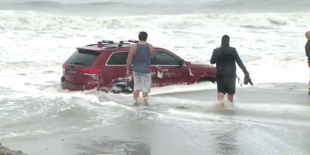 People can be seen taking pictures of the stuck Jeep before being cleared out of the area by police.