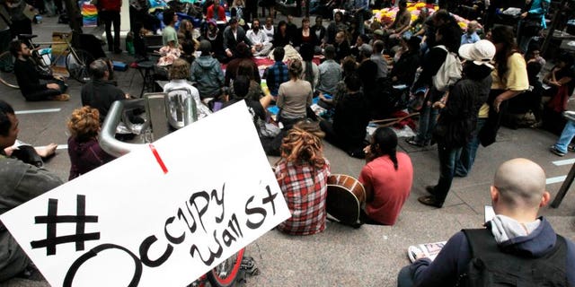 FILE – Occupy Wall Street protesters meditate while a sign bearing their twitter handle hangs from a railing in Zuccotti Park in New York October 1, 2011. REUTERS/Jessica Rinaldi