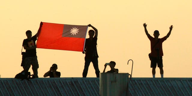 FILE - In this Sept. 14, 2014, file photo, locals on a warehouse rooftop display the national flag while watching Taiwan fighter jets practice during military exercises in Chiayi, central Taiwan. (AP Photo/Wally Santana, File)