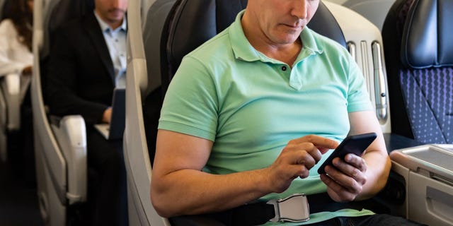 Man traveling by plane and using his cell phone onboard 