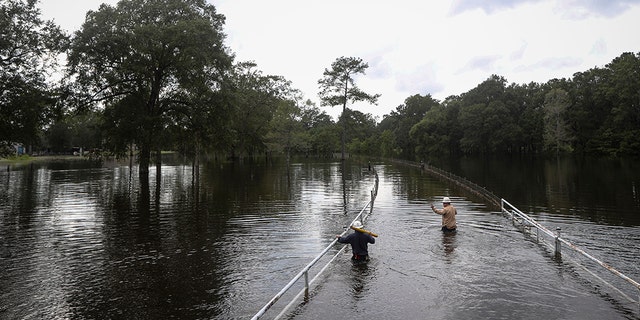 Mike Davis, left, and Trent Tipton, both line workers from Woodville, Texas, walk through floodwater to try to restore power for a customer on Friday, Sept. 20, 2019, in the Mauriceville, Texas, area. Floodwaters are starting to recede in most of the Houston area after the remnants of Tropical Storm Imelda flooded parts of Texas. ( Jon Shapley/Houston Chronicle via AP)