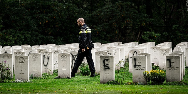 A police officer walks past graves which have been vandalized with graffiti, and a large swastika was daubed on the inner wall of the chapel in the British World War II Commonwealth Graves cemetery in Mierlo, east of Eindhoven, Netherlands, on September 13, 2019. (ROB ENGELAAR/AFP/Getty Images)