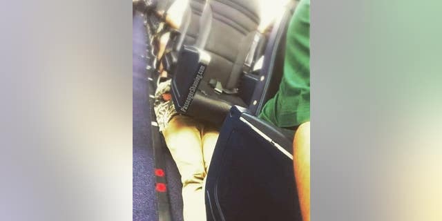 A passenger was seen laying down on an airplane floor, tucked underneath several seats on an unknown airline.
