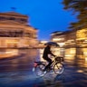 A man with an umbrella rides his bike in front of the Old Opera House in Frankfurt, Germany, Sept. 23, 2019.