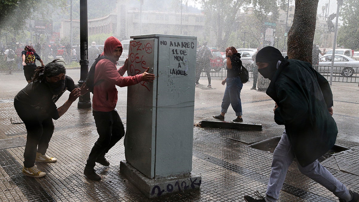 Demonstrators run for cover from a police water cannon during a protest in Santiago, Chile, Saturday, Oct. 19, 2019. (Associated Press)