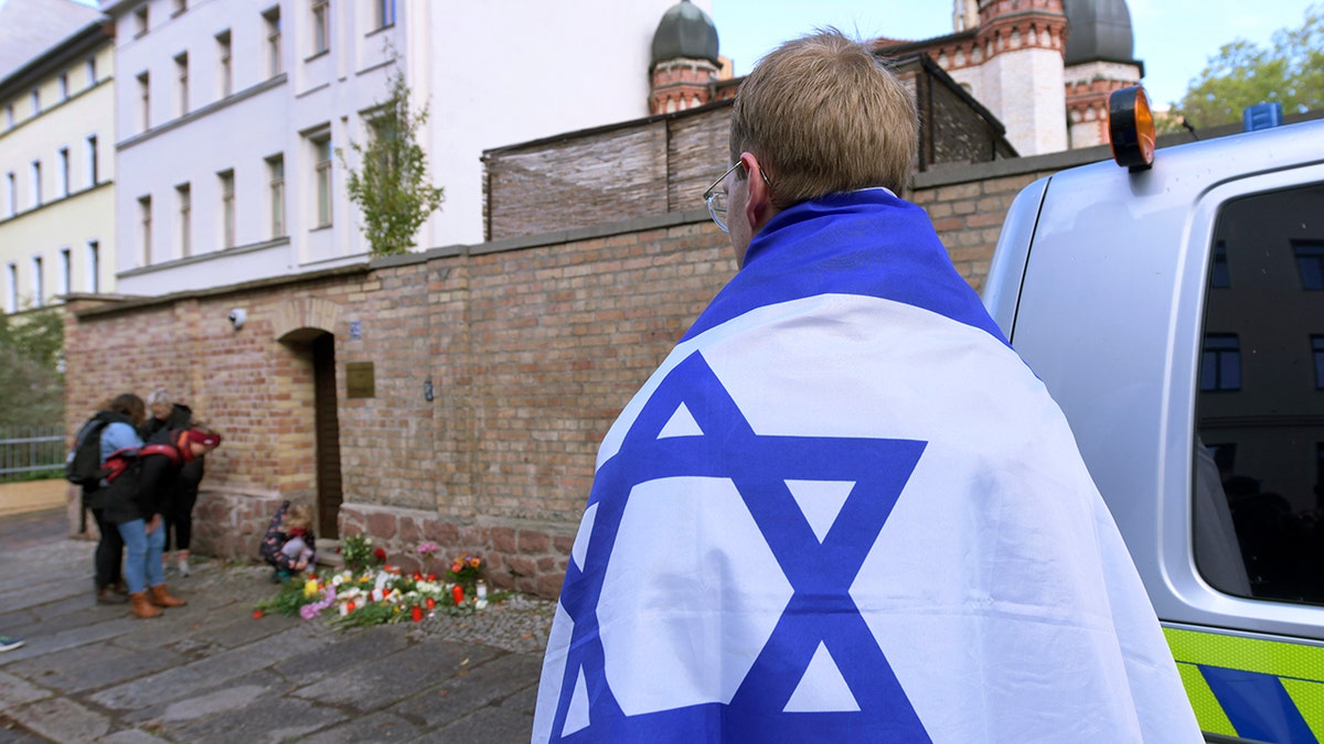 A person draped with the flag of Israel stands next to flowers and candles in front of a synagogue in Halle, Germany, on Thursday.