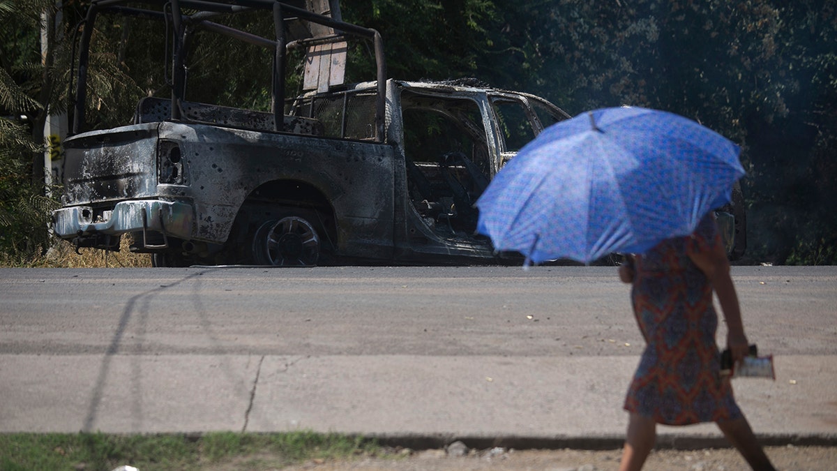 A pedestrian walks past a charred truck that belongs to Michoacan state police, after it was burned during an attack in El Aguaje, Mexico, Monday, Oct. 14, 2019.