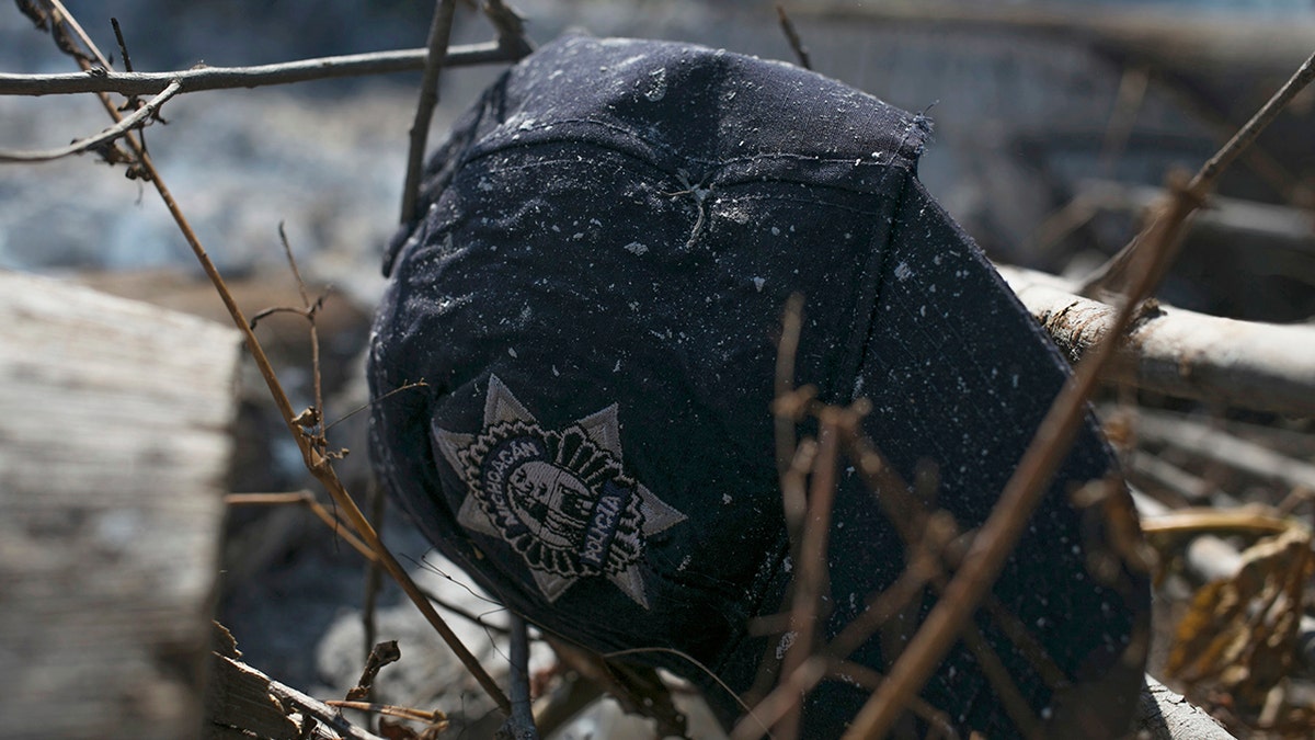 The cap of a Michoacan state police officer lies in the brush where charred police trucks stand on the roadside after its police officer occupants were attacked in El Aguaje, Mexico, Monday, Oct. 14, 2019.