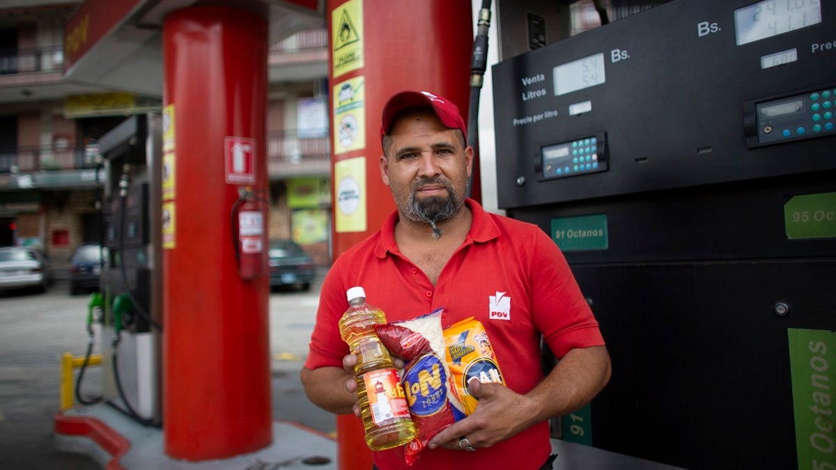 In this Oct. 8, 2019 photo, gas station attendant Leowaldo Sanchez poses with food items he was paid with by motorists: a bottle of cooking oil, a kilogram of rice and a package of corn flour, as he works at the pump in San Antonio de los Altos on the outskirts of Caracas, Venezuela. Bartering at the pump has taken off as hyperinflation makes Venezuela’s paper currency, the bolivar, hard to find and renders some denominations all but worthless, so that nobody will accept them. (AP Photo/Ariana Cubillos)