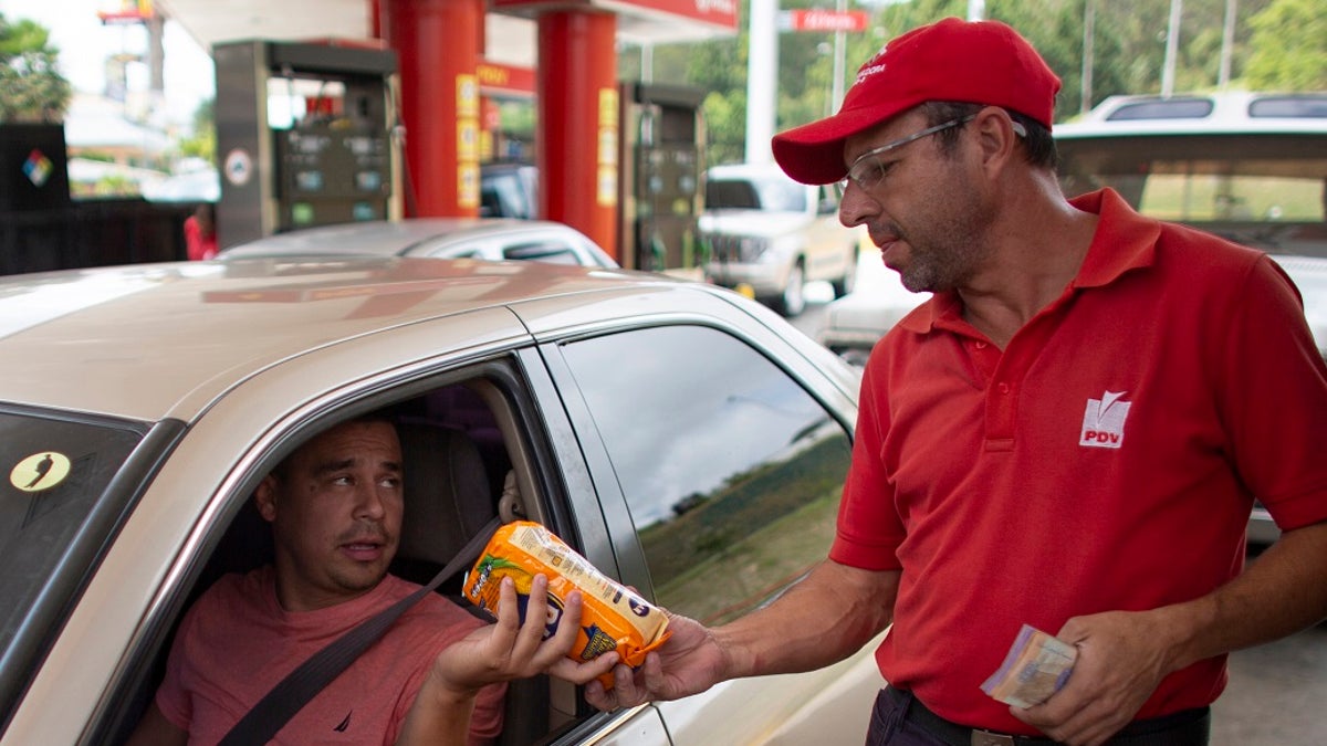 In this Oct. 8, 2019 photo, gas station attendant Orlando Godoy takes a package of corn flour as payment after filling a motorist's tank, which costs a tiny fraction of a U.S. penny, in San Antonio de los Altos on the outskirts of Caracas, Venezuela. The economy is in such shambles that drivers are now paying for fill-ups with a little food, a candy bar or just a cigarette. (AP Photo/Ariana Cubillos)