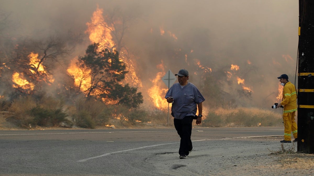 A man walks along Sierra Highway as flames from a wildfire overtake a hillside Thursday, Oct. 24, 2019, in Santa Clarita, Calif. The flames are fed by dry winds that are predicted to strengthen throughout the day across the region. (AP Photo/Marcio Jose Sanchez)