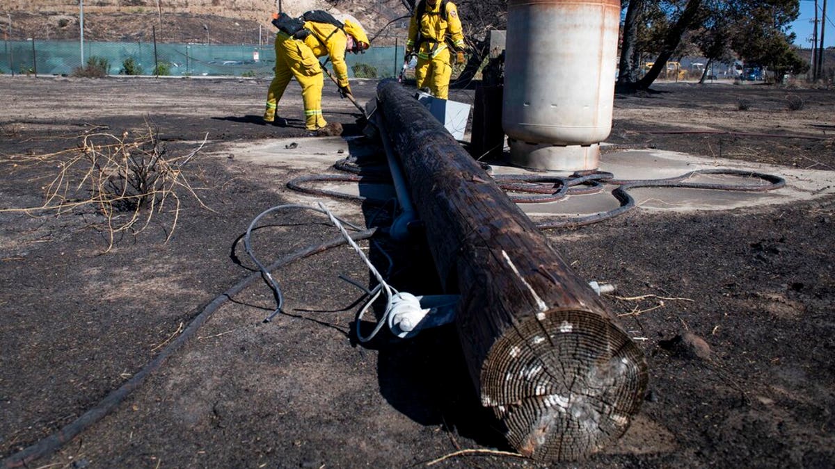 Firefighters with Cal Fire examine a burned down low voltage power pole during the Tick Fire, Thursday, Oct. 25, 2019, in Santa Clarita, Calif. An estimated 50,000 people were under evacuation orders in the Santa Clarita area north of Los Angeles as hot, dry Santa Ana winds howling at up to 50 mph (80 kph) drove the flames into neighborhoods (AP Photo/ Christian Monterrosa)