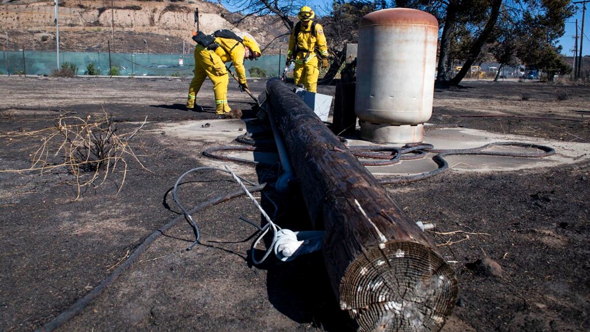 Firefighters with Cal Fire examine a burned down low voltage power pole during the Tick Fire, Thursday, Oct. 25, 2019, in Santa Clarita, Calif. An estimated 50,000 people were under evacuation orders in the Santa Clarita area north of Los Angeles as hot, dry Santa Ana winds howling at up to 50 mph (80 kph) drove the flames into neighborhoods?(AP Photo/ Christian Monterrosa)