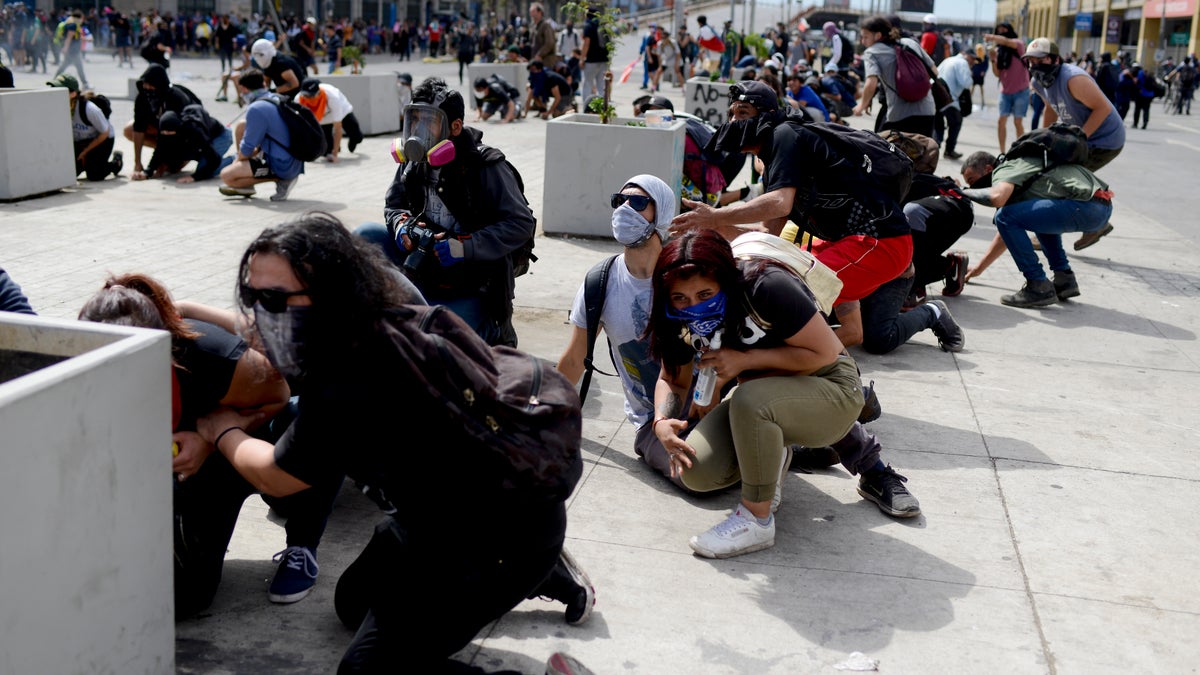 Anti-government protesters take cover just around the corner from the Congress building, during clashes with police in Valparaiso, Chile, Friday, Oct. 25, 2019. A new round of clashes broke out Friday as demonstrators returned to the streets, dissatisfied with economic concessions announced by the government in a bid to curb a week of deadly violence.(AP Photo/Matias Delacroix)